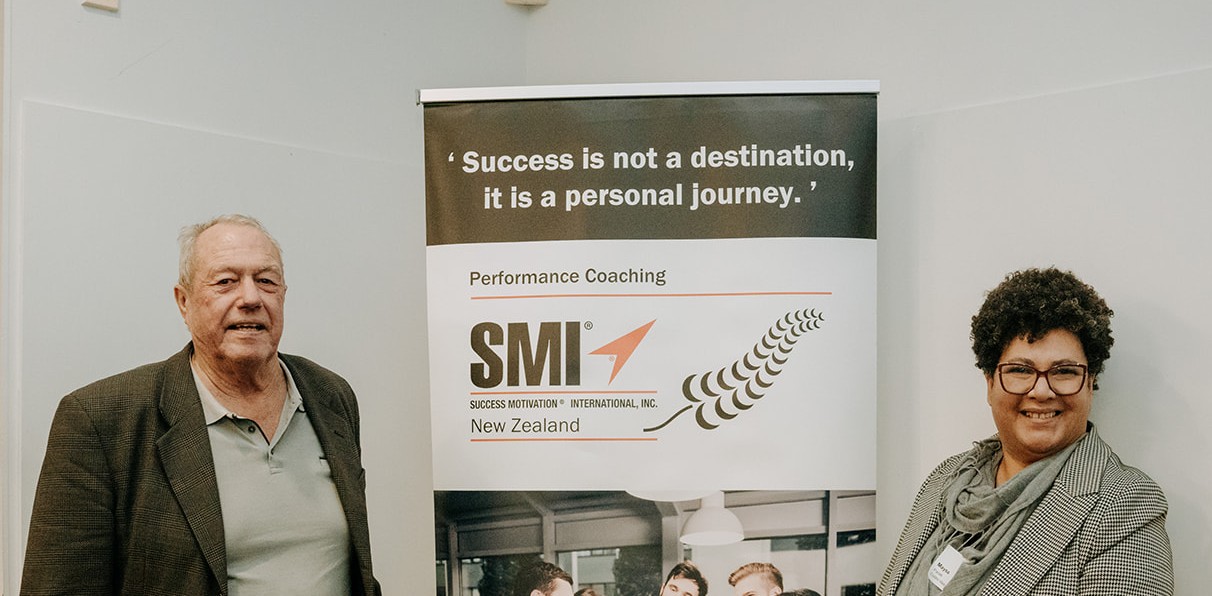 Roger Evans standing beside an SMI New Zealand Performance Coaching banner with another attendee.